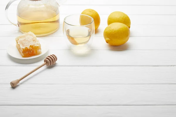 Bule transparente e vidro com chá verde, limões, favo de mel e gotejador de mel de madeira na mesa branca — Fotografia de Stock