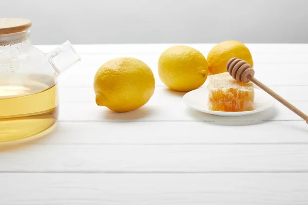 Teiera trasparente con tè verde, limoni e favo su tavolo di legno bianco — Foto stock