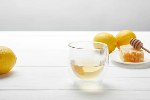 Transparent glass with green tea, lemons and honeycomb on white wooden table — Stock Photo