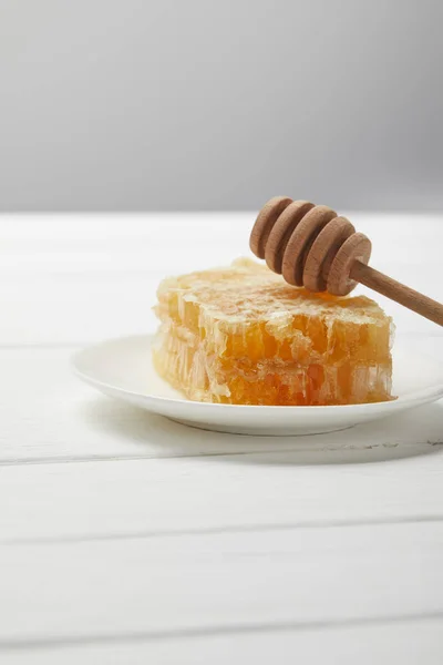 Prato com gotejador de mel e delicioso favo de mel em mesa de madeira branca isolada em cinza — Fotografia de Stock