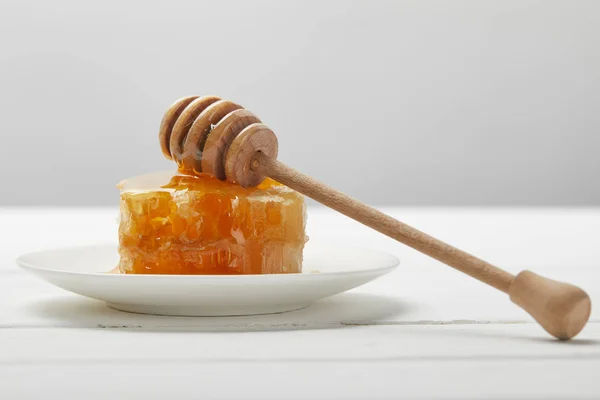 Assiette avec goutteur de miel et délicieux nid d'abeille sur table en bois blanc isolé sur gris — Photo de stock