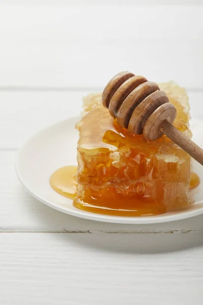 Enfoque selectivo de la placa con gotero de miel y delicioso panal en mesa de madera blanca - foto de stock