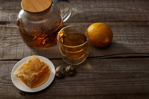 Limón, panal y tetera transparente con vaso de té chino en flor sobre mesa de madera - foto de stock