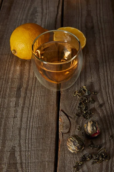 Glass of traditional chinese blooming tea, lemons and tea balls on wooden table — Stock Photo