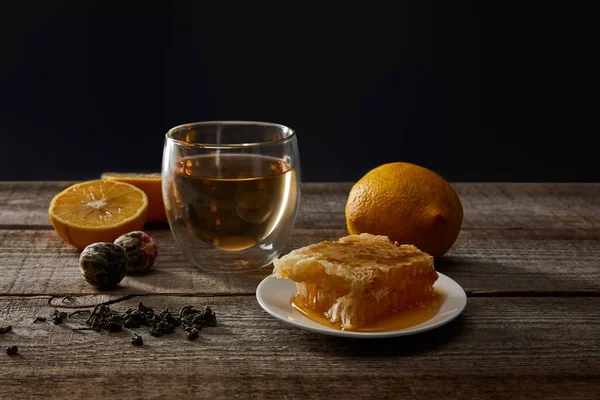 Vidrio transparente con té en flor, panal de abeja y limones en mesa de madera aislado en negro - foto de stock