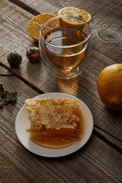 Glass of traditional chinese blooming tea, lemons and honeycomb on wooden surface — Stock Photo