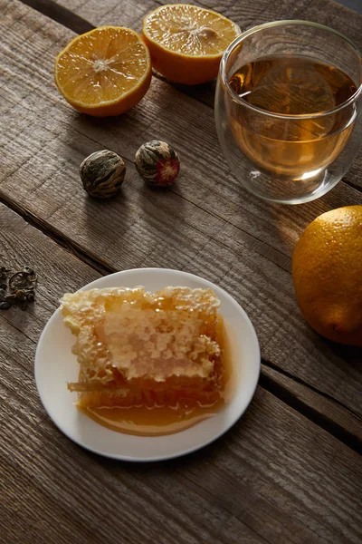 Glass of traditional chinese blooming tea, lemons and honeycomb on wooden table — Stock Photo