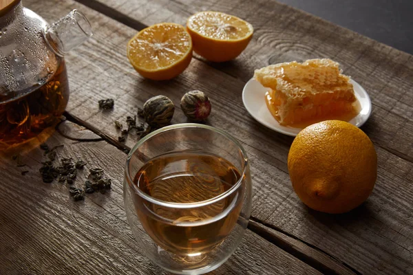 Bule transparente com vidro de chá chinês florescendo, favo de mel, bolas de chá e limões na mesa de madeira — Fotografia de Stock