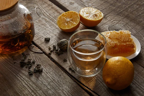 Lemons, honeycomb and transparent teapot with glass of traditional chinese blooming tea on wooden table — Stock Photo