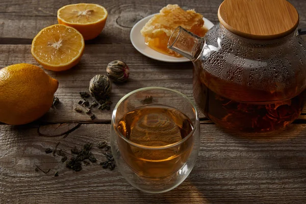 Lemons, honeycomb and transparent teapot with glass of chinese blooming tea on wooden surface — Stock Photo