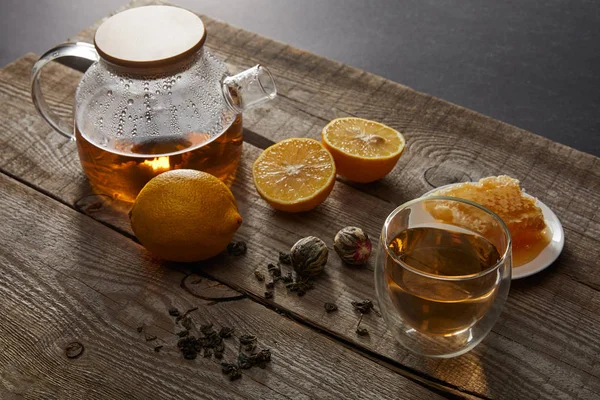 Limones, panal de abeja y tetera transparente con vidrio de té floreciente chino en superficie de madera - foto de stock