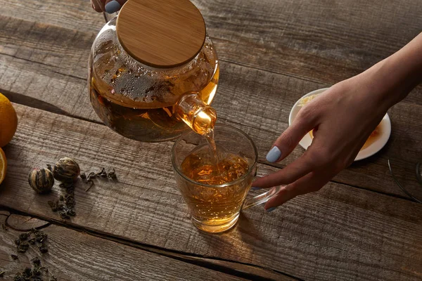 Cropped view of young woman pouring chinese blooming tea in cup on wooden table — Stock Photo