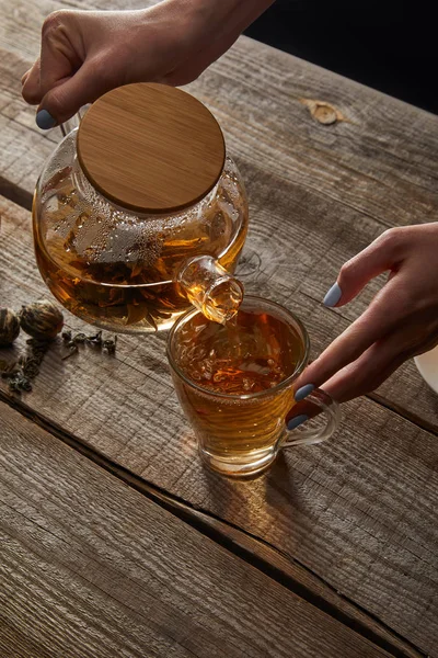 Vista cortada da jovem mulher derramando chá chinês florescendo na xícara na mesa de madeira — Fotografia de Stock