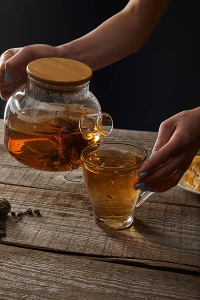 Cropped view of young woman pouring blooming tea from teapot in cup isolated on black — Stock Photo