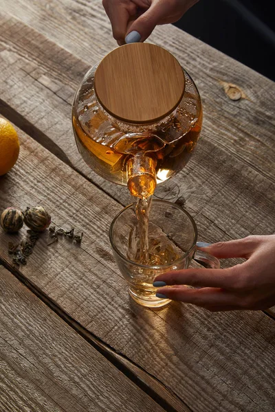 Vista recortada de la joven mujer vertiendo té tradicional chino en flor en taza en la mesa de madera - foto de stock