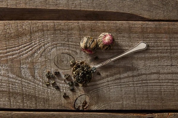 Top view of spoon with green tea and blooming tea balls on wooden table — Stock Photo