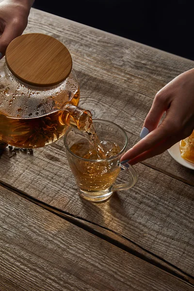 Abgeschnittene Ansicht einer jungen Frau, die traditionellen chinesischen blühenden Tee in Tasse auf Holztisch gießt — Stockfoto