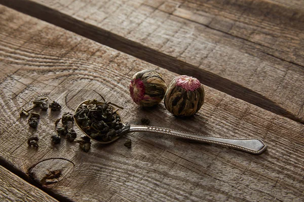 Spoon with green tea and blooming tea balls on wooden table — Stock Photo