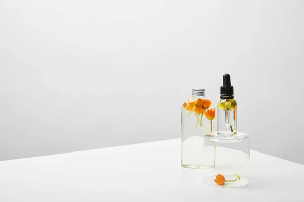 Bottle with organic shampoo and orange flowers near natural serum on transparent stand on white table — Stock Photo