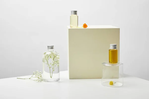 Bottles with organic cosmetics and flowers on white table on grey background — Stock Photo