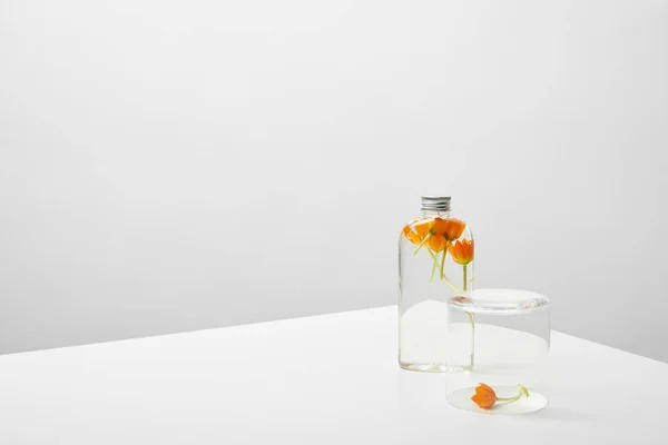 Bottle with organic beauty product and orange wildflowers on white table on grey background — Stock Photo