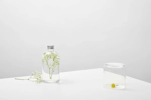 Bottle with natural beauty product and white wildflowers on grey background — Stock Photo