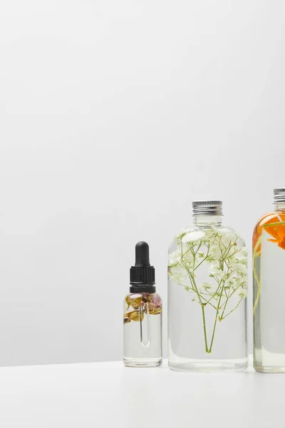 Different organic beauty products in bottles with herbs and flowers on grey background — Stock Photo