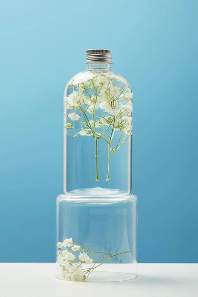 Prodotto cosmetico biologico in bottiglia trasparente con fiori selvatici isolati su blu — Foto stock
