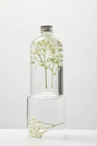 Produto cosmético orgânico em garrafa transparente com flores silvestres em stand isolado em cinza — Fotografia de Stock