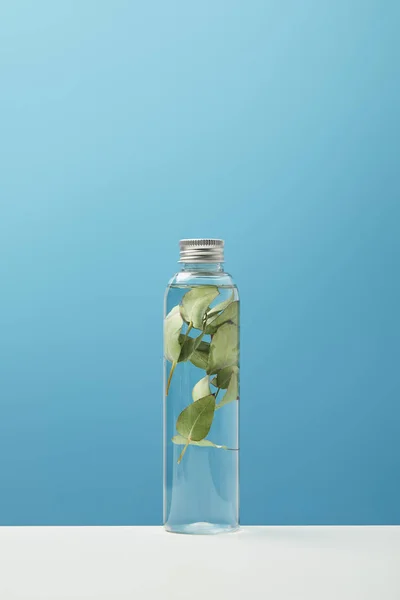 Organic cosmetic product with green leaves in transparent bottle on white table isolated on blue — Stock Photo