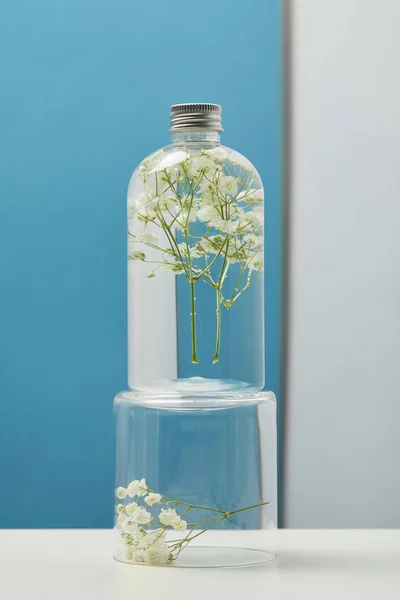 Organic cosmetic product with white wildflowers in transparent bottle — Stock Photo