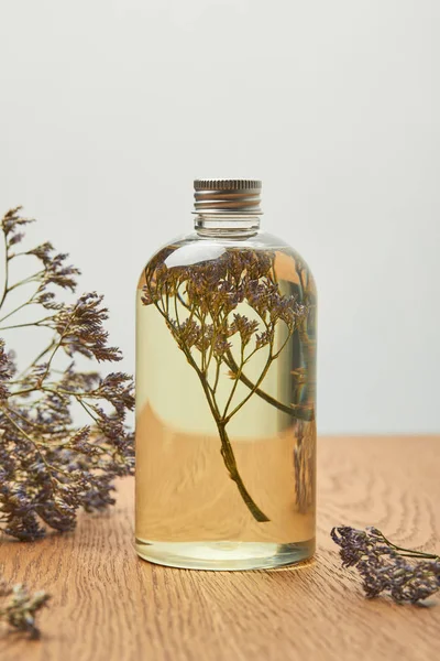 Natural beauty product in bottle near purple dried wildflowers on wooden table isolated on grey — Stock Photo