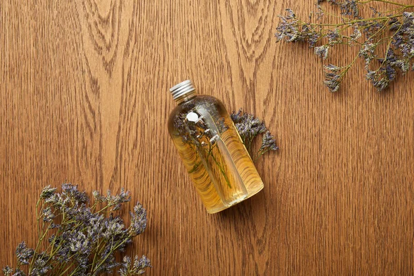 Top view of transparent bottle with natural beauty product near dried herbs on wooden background — Stock Photo