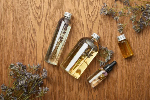 Top view of transparent bottles with organic beauty products near dried herbs on wooden background — Stock Photo