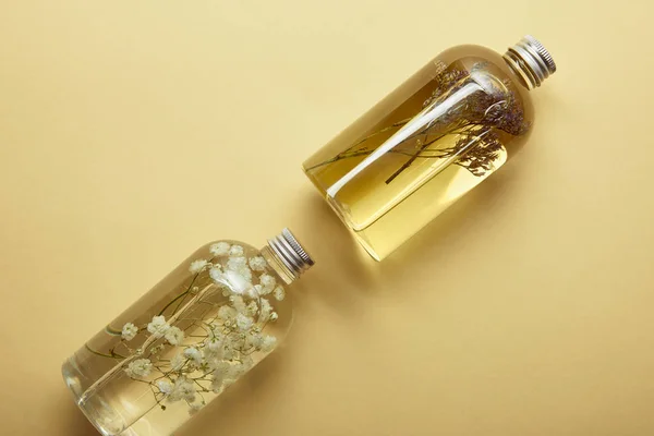 Вид зверху на прозорі пляшки з органічними продуктами краси та сушеними лісовими квітами на жовтому фоні — стокове фото