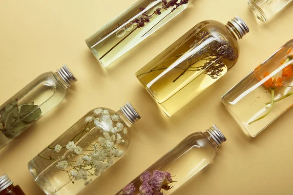 Vista superior de botellas transparentes con productos orgánicos de belleza y flores silvestres secas y hierbas sobre fondo amarillo - foto de stock