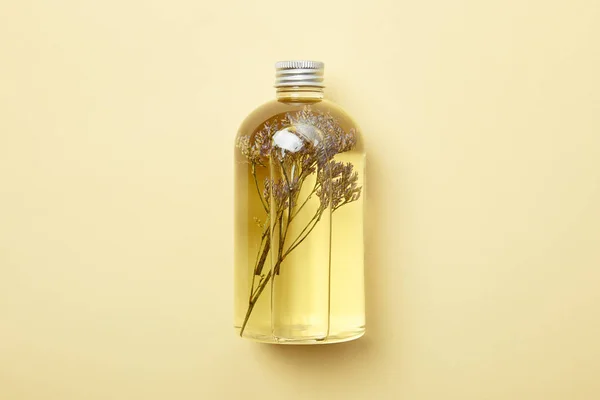 Vista superior de la botella con producto de belleza orgánica y flores silvestres secas sobre fondo amarillo - foto de stock