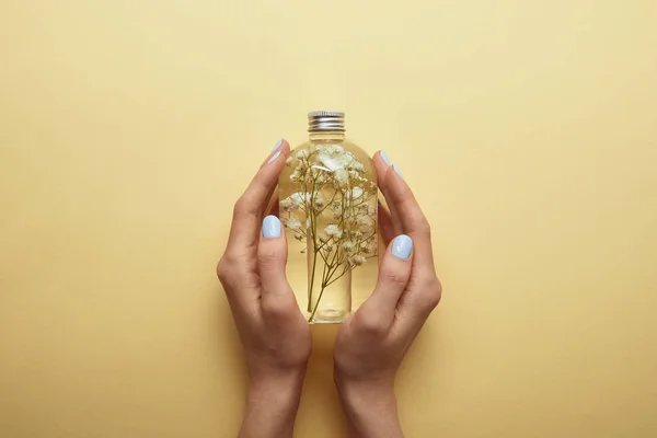 Vue partielle de la femme tenant bouteille avec des produits de beauté naturels et des herbes dans les mains sur fond jaune — Photo de stock