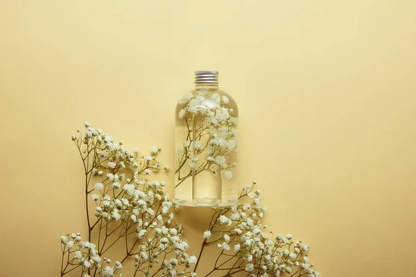 Vista superior da garrafa com produto de beleza orgânica perto de flores silvestres brancas secas no fundo amarelo — Fotografia de Stock