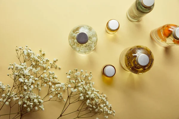 Vista superior de botellas con tapas, productos orgánicos de belleza y flores silvestres secas sobre fondo amarillo - foto de stock