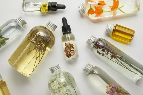 Vista superior de garrafas transparentes com produtos de beleza natural e flores silvestres secas em fundo cinza — Fotografia de Stock