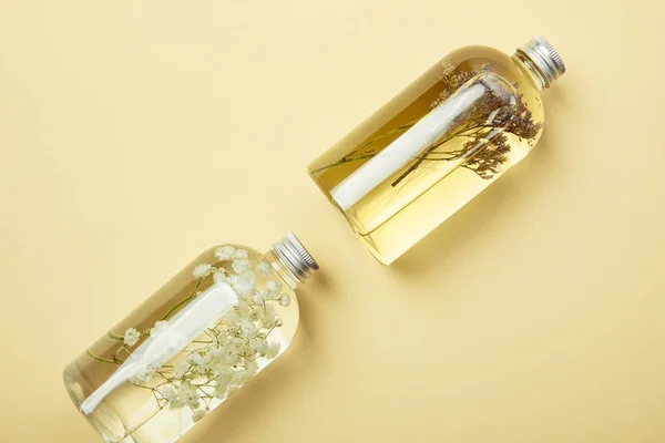 Vue du dessus des bouteilles transparentes avec des produits de beauté liquides naturels et des fleurs sauvages sur fond jaune — Photo de stock