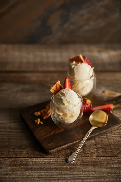 Délicieuse crème glacée dans des verres avec des fraises et des morceaux de gaufre sur la planche à découper sur la table — Photo de stock