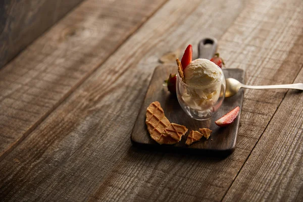 Delicious ice cream with strawberries in glass and pieces of waffle on wooden table — Stock Photo