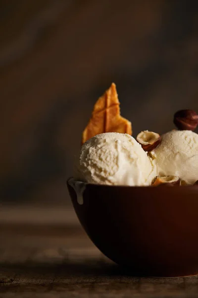 Selective focus of delicious ice cream scoops with piece of waffle and hazelnuts in bowl on table — Stock Photo