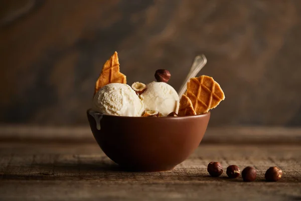 Savoureuses boules de crème glacée avec des morceaux de gaufres et noisettes dans un bol sur une table en bois — Photo de stock