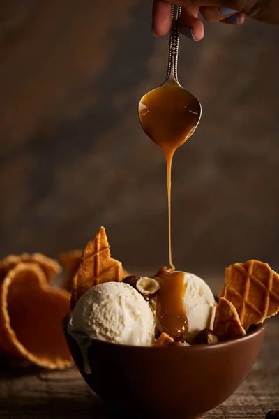 Vue recadrée de la femme versant du caramel sur une crème glacée avec des morceaux de gaufres et de noisettes — Photo de stock