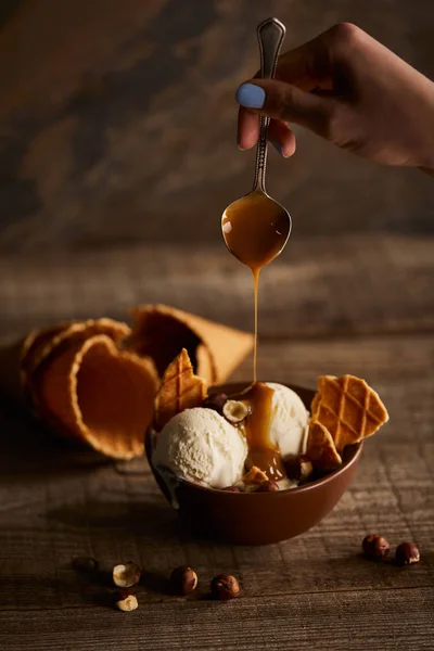 Visão parcial da mulher derramando caramelo em delicioso sorvete com pedaços de waffle na tigela — Fotografia de Stock