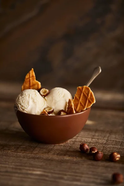 Deliciosas colheres de sorvete com pedaços de waffle e avelãs em tigela na mesa de madeira — Fotografia de Stock