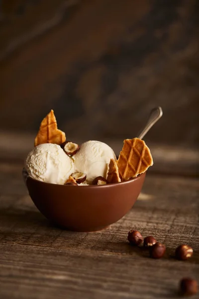 Leckere Eiskugeln mit Waffelstücken und Haselnüssen in Schüssel auf Holztisch — Stockfoto